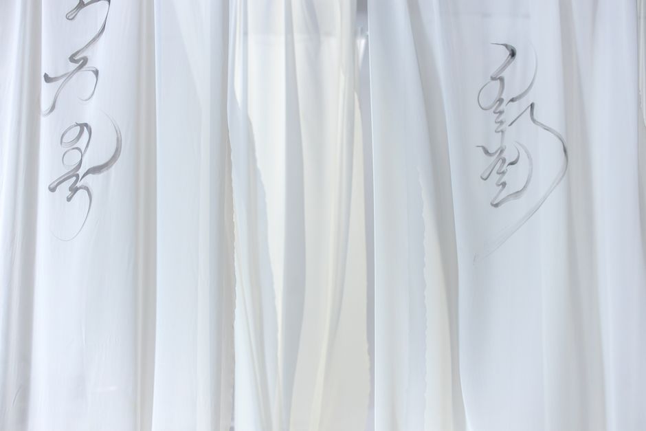 Minimalist photo featuring delicate black ink calligraphy on flowing white curtains, with ample copy space.
